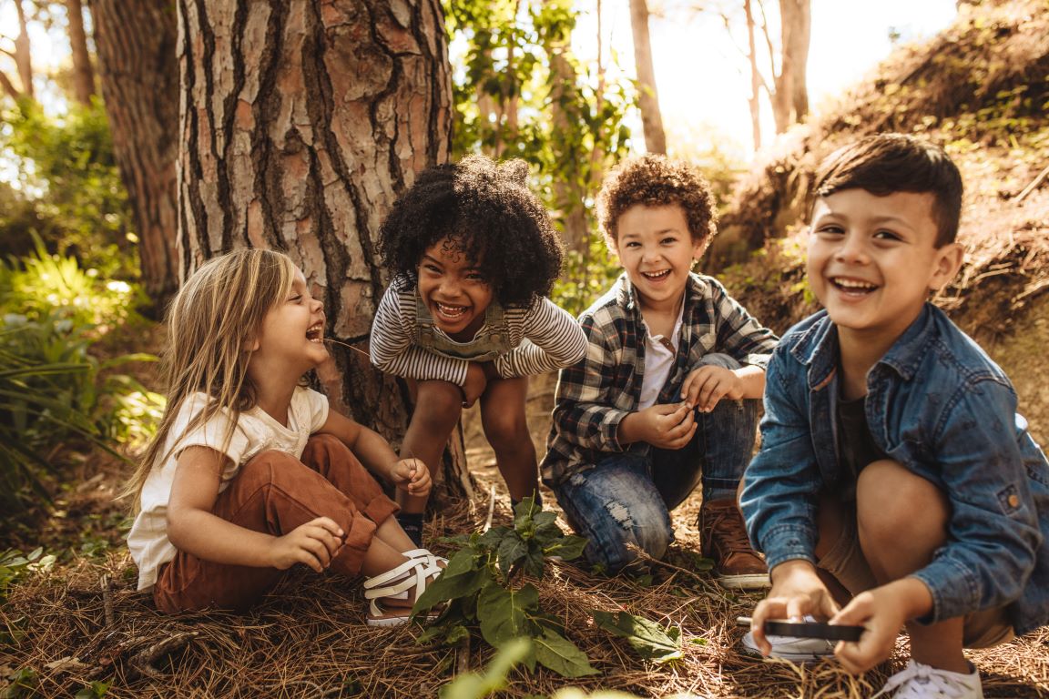 Four laughing children playing together in a forest.